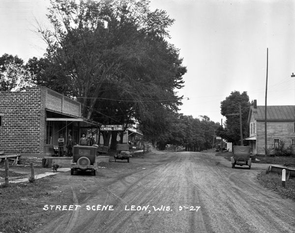 View down road towards a group of men posing on the porch of Young's general store.