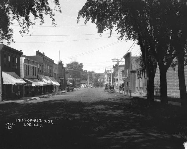 View down shady Lodi Street. The shops further along the street include: a laundry service, People's Clothing Store, E.N. Davis Furniture, Gates Brother's Lumber, and a livery and feed stable.