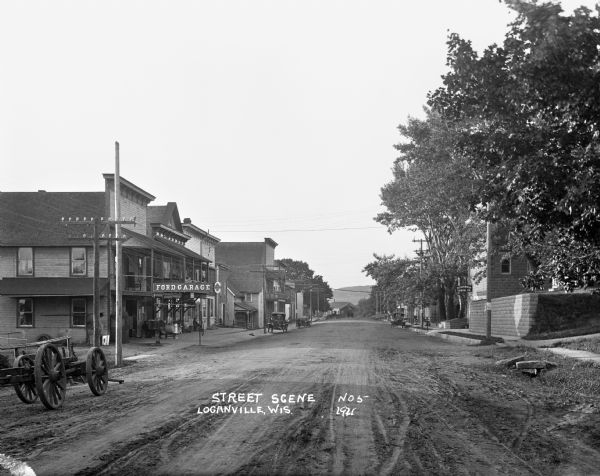 View down an unpaved street. There is a Ford automotive repair garage on the left side of the street.