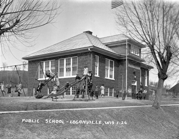 Children play on slides, see-saws, and swings in the playground of the public school.