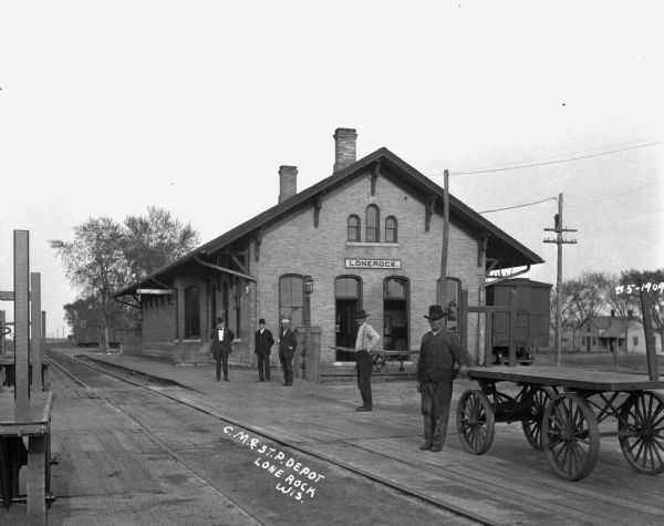 Five men stand on the platform of the Lone Rock depot waiting for the train.
