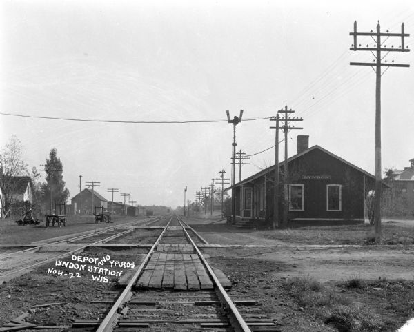 View down center of railroad tracks with the Lyndon depot on the right. Carriages and carts are along both sides of the tracks.