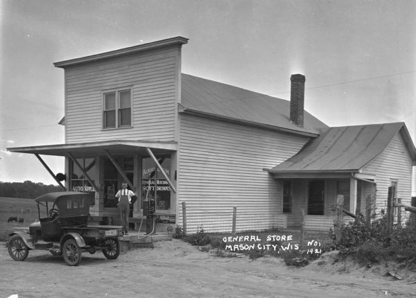 A man poses on the porch of a general store and filling station.