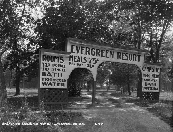 The entrance way to the Evergreen Resort. The sign advertises rooms, hot and cold water baths, meals, camp sites, and tourist kitchens. Caption reads: "Evergreen Resort — On Highway 12-16 — Mauston, Wis."