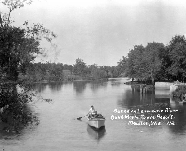 Slightly elevated view towards a man rowing his boat along the Lemonweir River. Caption reads: "Scene on Lemonweir River — Oak & Maple Grove Resort — Mauston, Wis."