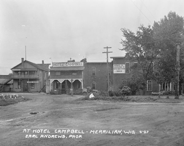 View from road of a man standing in front of the Campbell Hotel, located next door to the Lunch Room. Earl Andrews is listed as the proprietor. A sign painted on the hotel building reads, "Entrance for automobiles to Hotel and Lunch Room - Drive-in."