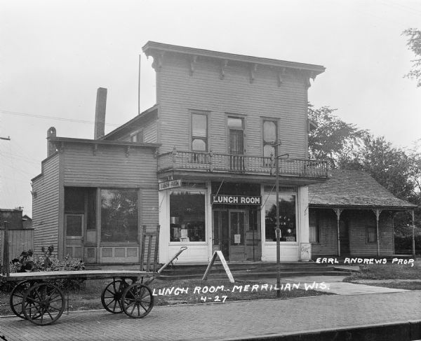 View of the facade of the Lunch Room restaurant, located near a cobblestone train platform. Earl Andrew is listed as the proprietor.