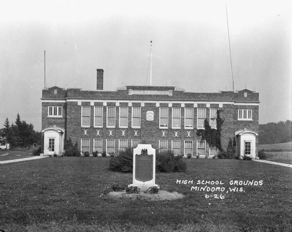 Exterior view of the Mindoro high school and grade school, housed in the same two-story, brick building. A plaque in front of the school commemorates Farmington [?] honor roll students. A plaque on the building says: "1921."