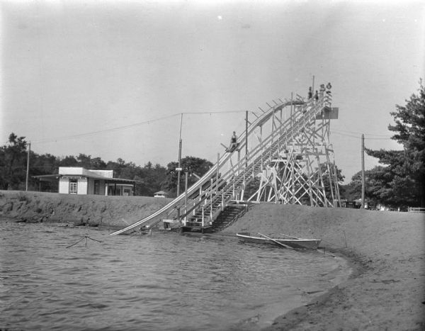 View from shoreline of a water slide at Mirror Lake State Park. A woman rides down the slide into the lake, and a few people stand on the platform behind her.