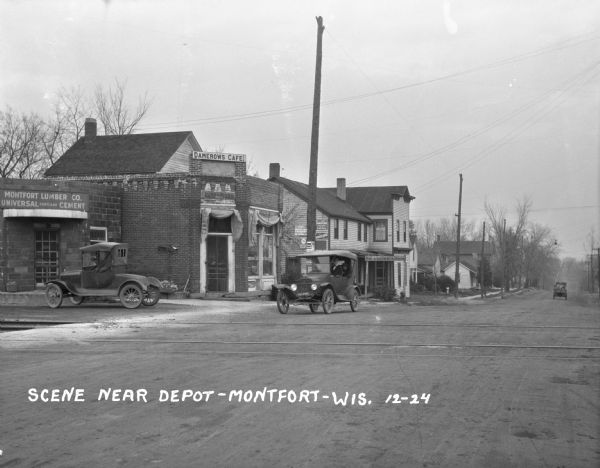 View across railroad tracks of storefronts located near the train depot. The shops include: Montford Lumber Company, Damerow's Cafe, and the American Hotel.