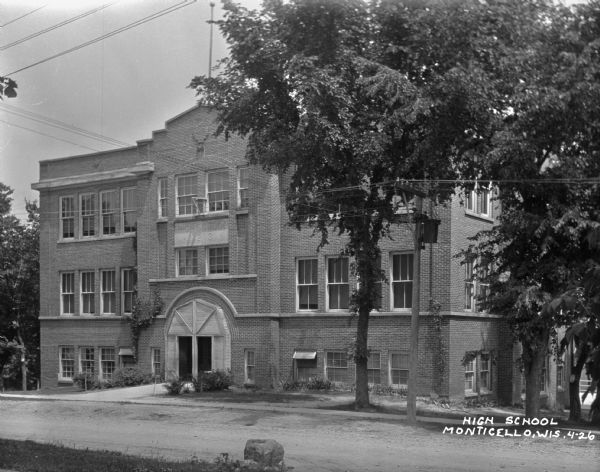 View from across road of the exterior of the three-story high school. A datestone above the arched entrance reads: "High School 1913". Caption reads: "High School Monticello, Wis."