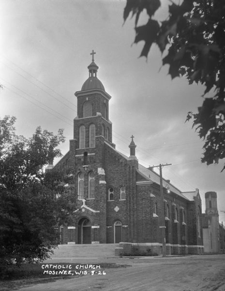 Exterior of Saint Paul's Catholic Church. Tree leaves cover the top-right corner of the image. There is a street sign for "Fourth St." on a power line pole near the church.