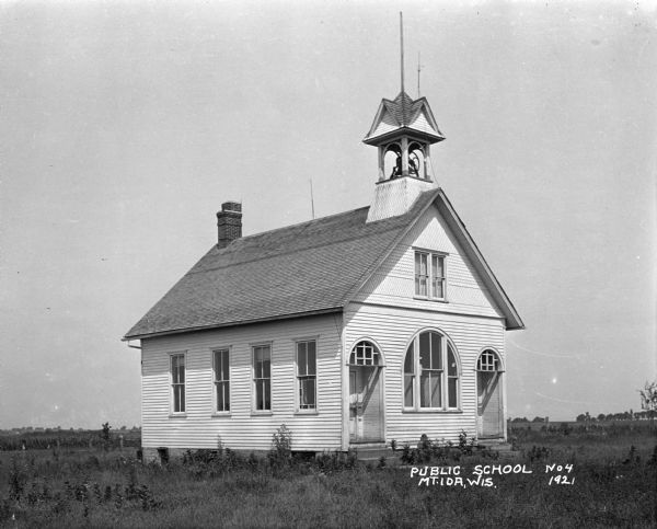 Exterior of the public schoolhouse, which features a bell tower and two arched entrances.