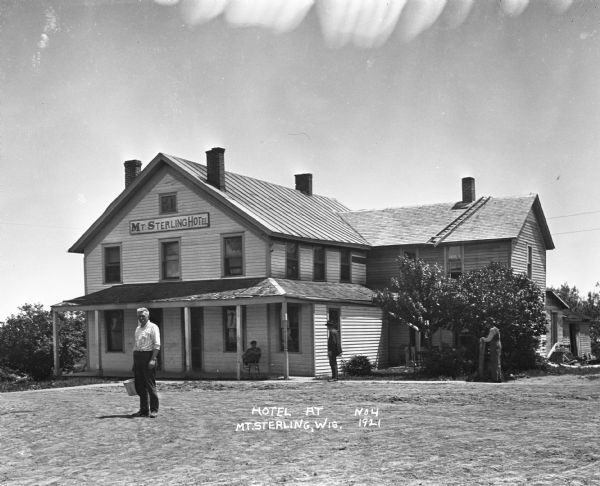A man holding a bucket stands outside the Mount Sterling Hotel. Three other men are in the background.