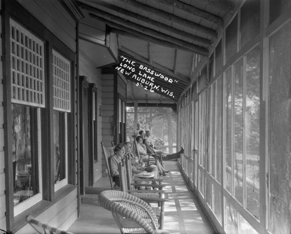 Vacationers sitting on wicker chairs on the enclosed porch at the Basswood in Long Lake.