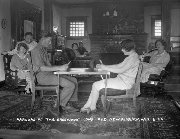 Vacationers in the parlor of the Basswood in Long Lake. A banner on the piano in the background says: "Northern Wis. State Fair."