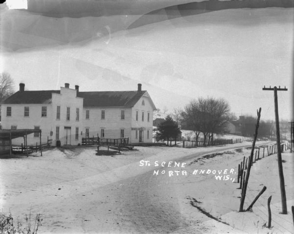 Two buildings, and what appears to be a stable, along a snow-covered road. The larger building has a sign that says "Hotel."
