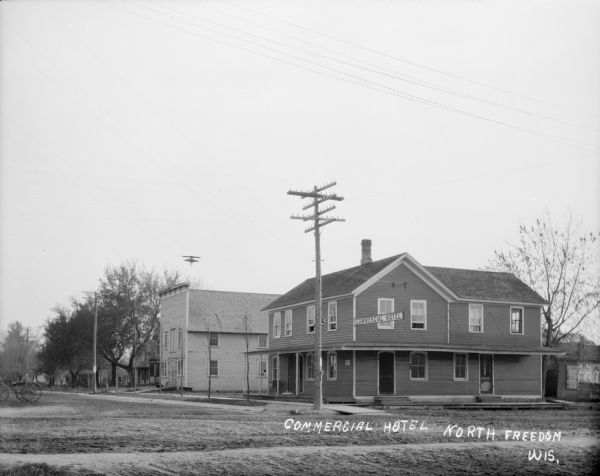 View from unpaved street of the Commercial Hotel on a corner. There is a wagon on the left.