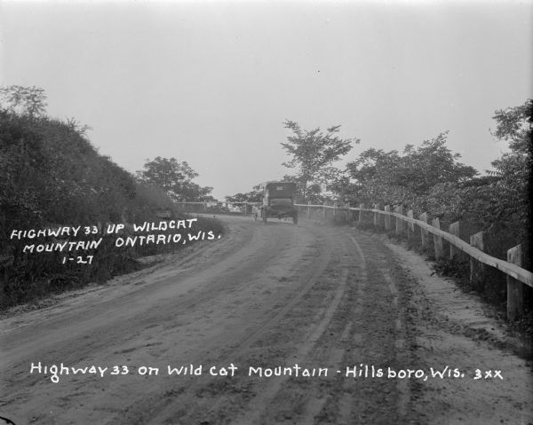 An automobile traveling up the dirt road to Wildcat Mountain. There is a guardrail along the road on the right.