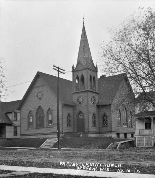 View from across street of the wooden Presbyterian Church with steeple. The round, stained glass windows on the steeple and the front of the church have a flower pattern. The windows on the first floor are arched.