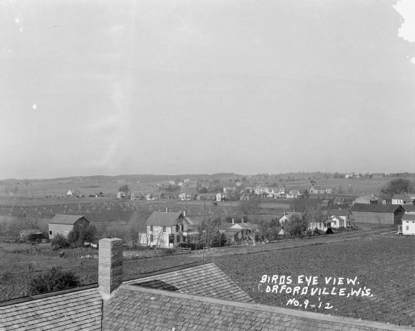 Elevated view over rooftops. Farm fields and houses are in the background.