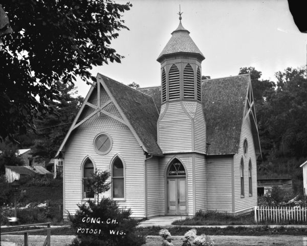 View of the exterior of the Congregational Church, with arched windows and belfry. In the arched window above the doorway it reads: "1891 Cong'l Church." In the background are houses and outbuildings.