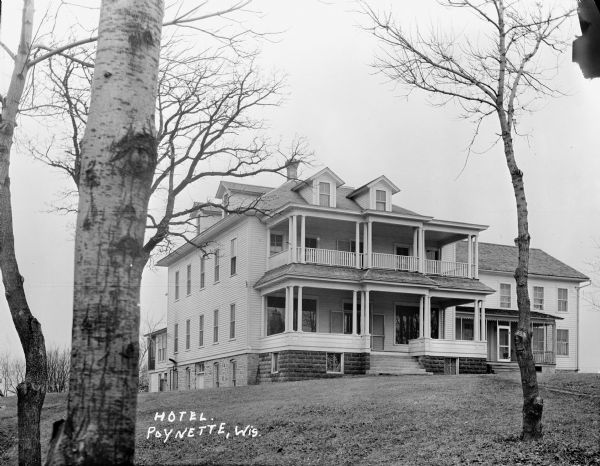 View across front lawn of a two-story hotel with porches and balconies. An addition built on the right side has a screened-in porch.