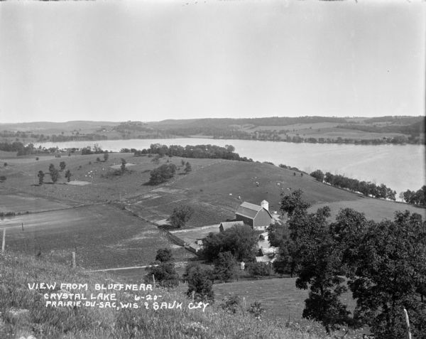 View from bluff of Crystal Lake and surrounding rolling hills. There is a dairy farm in the foreground at the bottom of the bluff. Cows are grazing in fields on the rolling hills.