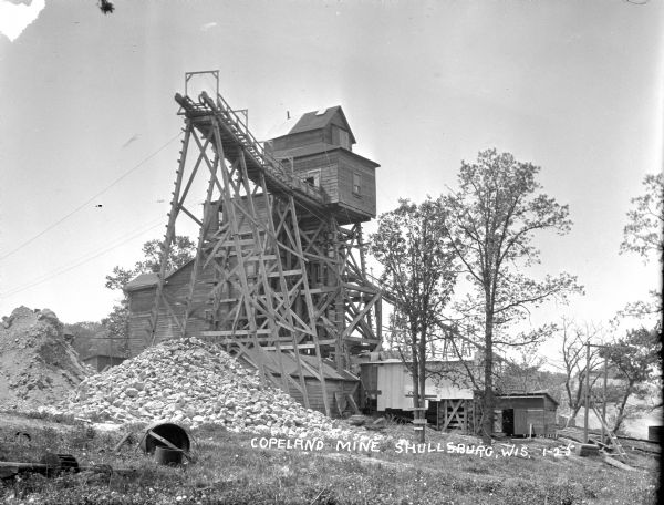 Exterior view of the Copeland Mine. Entry building, with tram tracks suspended high on scaffolding and piles of rocks below.