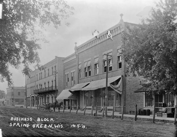 View from unpaved road of the Cohen Bros Dept. Store, D.N. Farris storefront, and Park Hotel. A soda fountain in another building is on the right. A team of horses pulling a cart is parked along the curb.
