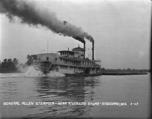View from right rear of the "General Allen" steamer pushing a barge on the Mississippi River. Smoke is pouring out of the two funnels at the front of the steamer. There are two men standing on the barge, and men are driving the steamer.