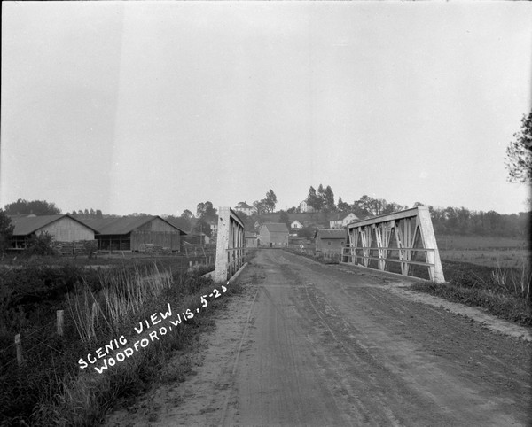 A view of a road crossing a bridge into a rural community. A railroad crossing at the far end.