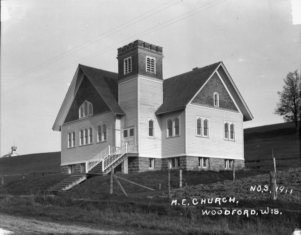 Three-quarter view of the Methodist Evangelical Church on a hillside. It has a belfry with no steeple and windows shaped like elongated pentagons.