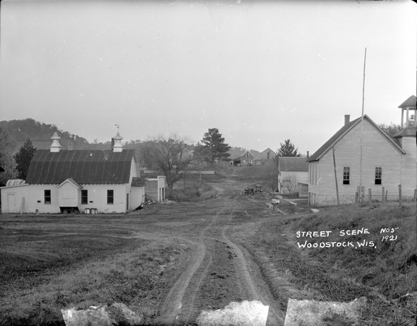 A view of a center street with a barn on the left and a school on the right.