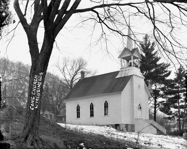 Three-quarter view of the Congregational Church, a wood structure with a belfry and steeple. There are arched windows and a flight of stairs to the entrance. Snow is on the hillside.
