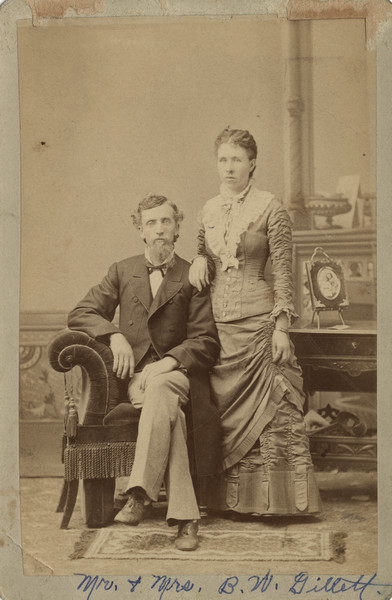 Portrait in front of a painted backdrop of Bradford and Alice Gillett, Sherwin Gillett's uncle and aunt. There is a framed portrait of two children on a table on the right.