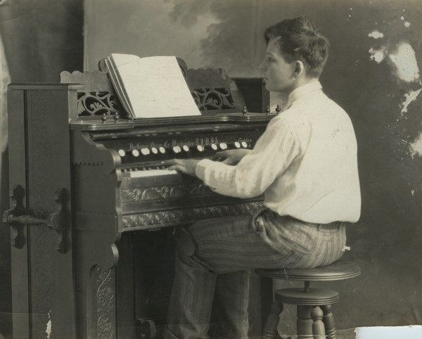 Sherwin Gillett's son Lorin playing an organ. He is posed in front of a painted backdrop. On the organ is written: "Beethoven Organ Co., Washington, N.J. U.S.A."