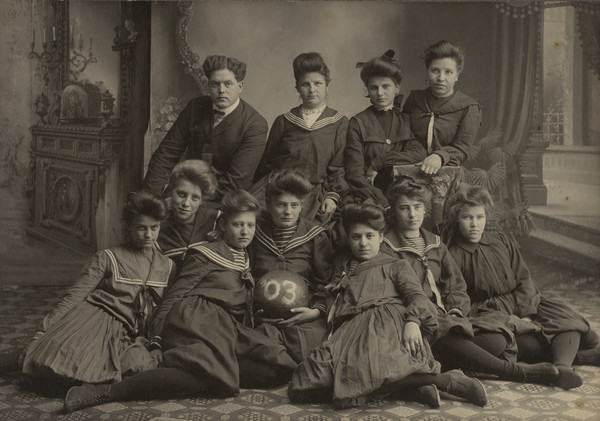 Group portrait in front of a painted backdrop of the Muscoda High School Girls' Basketball Team and their coach. The frame has the S. Gillett imprint, but the photograph is from years before he started his photography business in Muscoda.