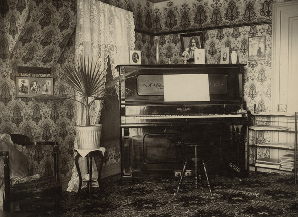 Interior view of the parlor of the Conrad Schmitt (Sherwin Gillett's father-in-law) home. Family photographs are on the wall and on the piano.