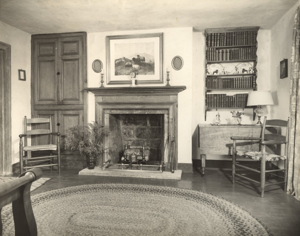 Interior view of a sitting room at Trelawny House, with period chairs, a bookcase and a painting of sheep above the fireplace.
