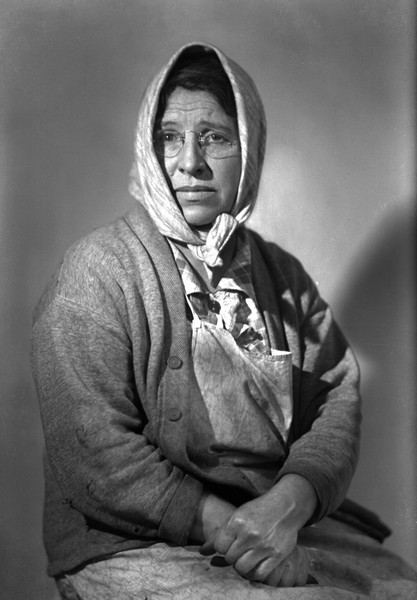 Waist-up portrait of Emma Gillett, wife of Sherwin, mother of Lorin. She is wearing a scarf over her head, an apron and a  sweater.