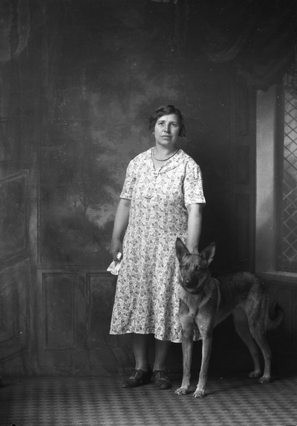 Full-length portrait in front of a painted backdrop of Emma Gillett with their German Shepherd, Monday.