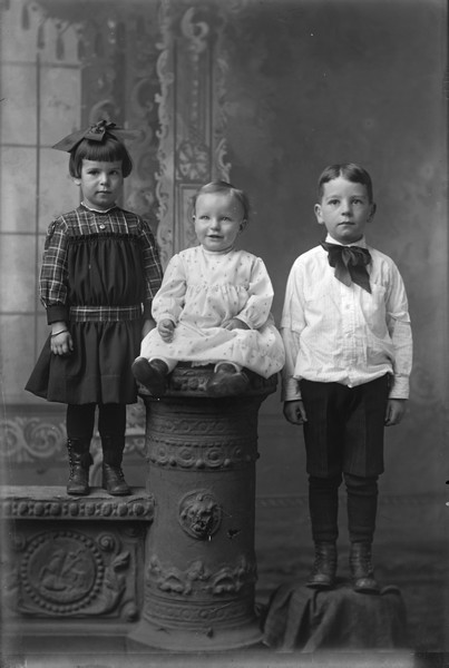 Studio group portrait in front of a painted backdrop of the Gillett children, left to right: Sherry (b. 1913), Lorin (b. 1915), and Harry (b. 1910).