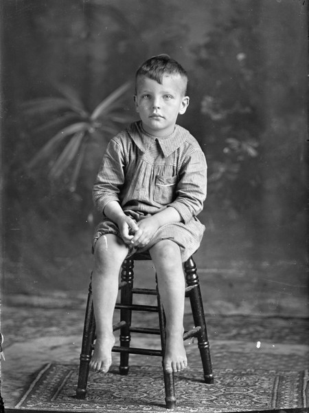 Studio portrait in front of a painted backdrop of young Lorin Gillett sitting on a stool.