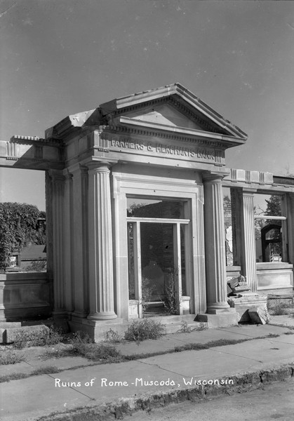 View from street of the Farmers and Merchants Bank after a fire. All that's left standing is its neo-classical marble facade with columns framing a doorway.