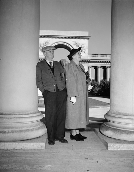Outdoor portrait of Sherwin and Emma Gillett standing between the columns at the Legion of Honor. Part of the marble arch is visible behind them.