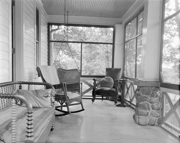 Screened-in porch at the Birchcliff Hotel, with chairs, porch swing and settees.