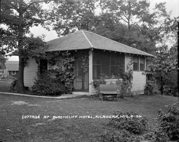 View across lawn of a guest cottage at the Birchcliff Hotel. A woman is seated in the screened-in porch.