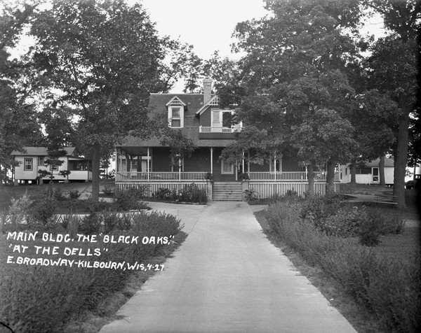 View up drive towards the main building with wrap-around porch. A bicycle is parked at the bottom of the stairs. Guest cottages are behind the main building.