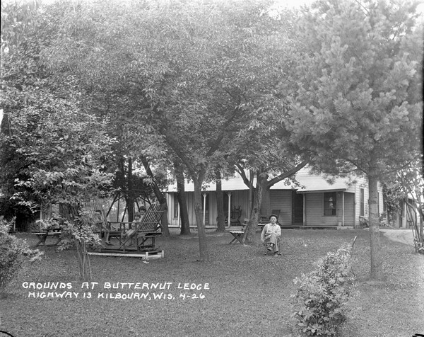 View across lawn of the main building and grounds at Butternut Lodge. Three young children are on are a lawn swing, and a man sits in a chair nearby.